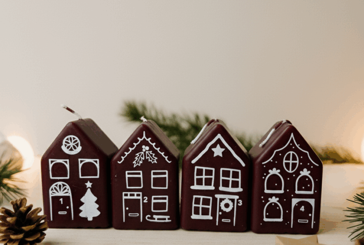 Set van vier rode advent kerstkaarsjes in de vorm van huisjes, gepresenteerd in Scandinavische stijl met natuurlijke kerstdecoratie.